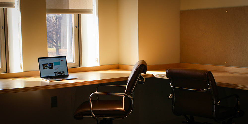 Laptop sitting on an empty desk as light shines through a window.